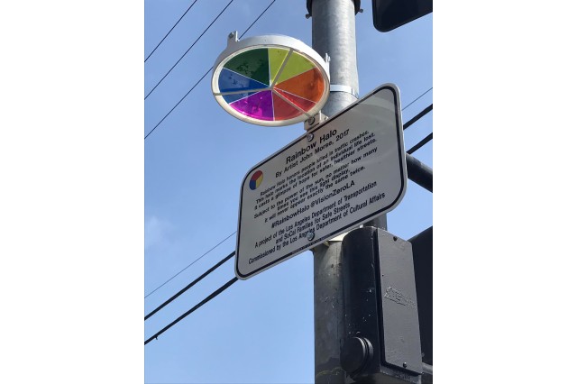 Circular multicolor reflector suncatcher attached perpendicular to an electrical pole above a sign describing these rainbow halos as a tribute to people killed in traffic crashes.