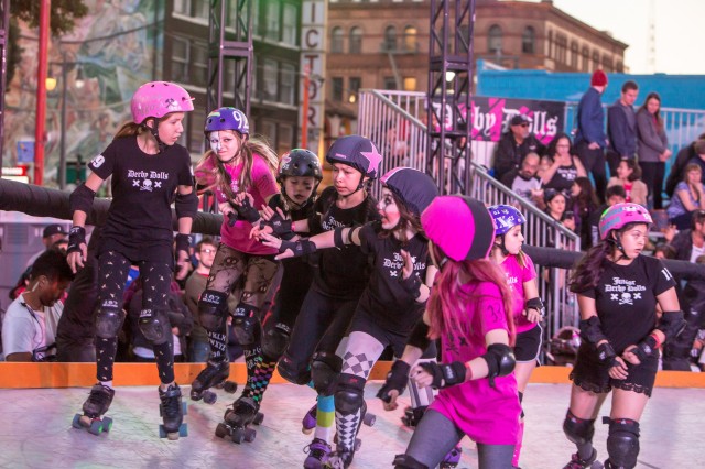 Young girls in pink vs. white uniforms skating in a roller derby bout