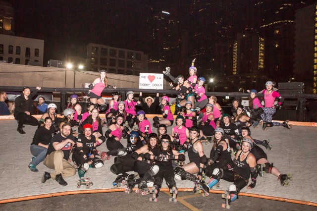 Large team photo of roller derby skaters in black and pink uniforms.