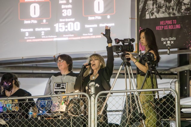 Evil E announcing a bout next to a film crew in front of the score board