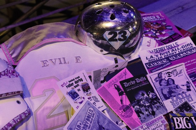 Table display of #23&#039;s roller derby silver helmet, pink jersey, and past event flyers