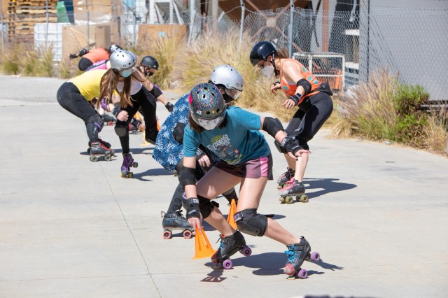 Young women in athletic gear practicing roller derby moves in a parking lot