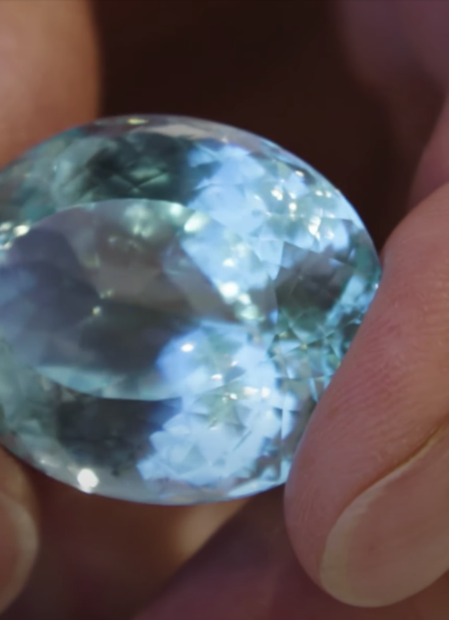 A hand hold an aquamarine colored gemstone