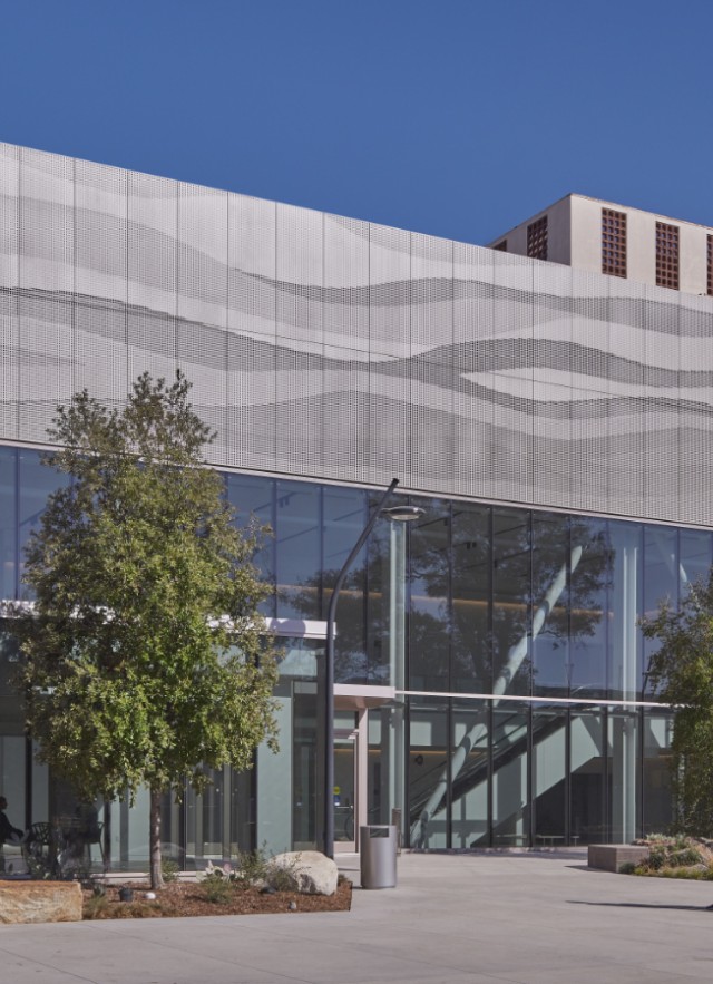 Two people walking towards a silver building with a wall of windows