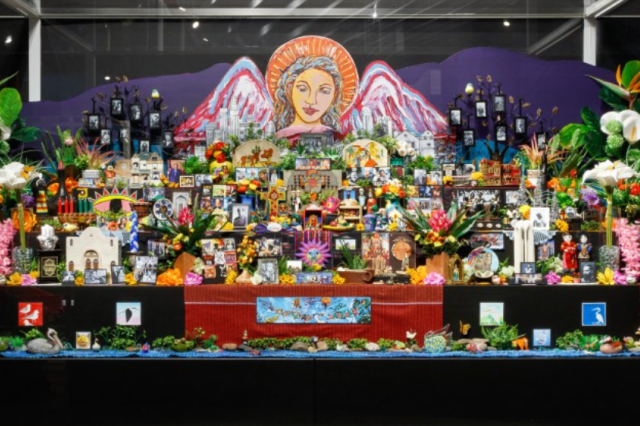 A paining of an angel looks over an altar filled with colorful objects