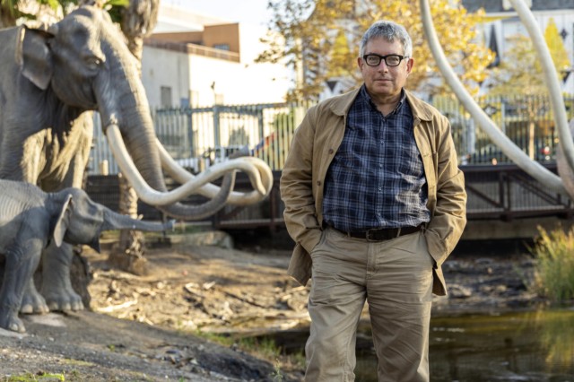 Mark Dion standing outside in front of mammoth sculptures and lake pit