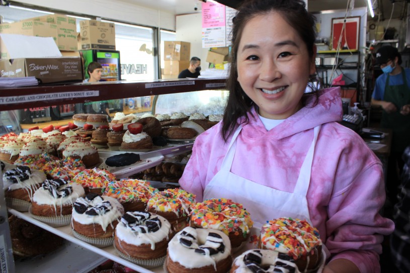 Woman in pick sweatshirt holding tray of donuts 